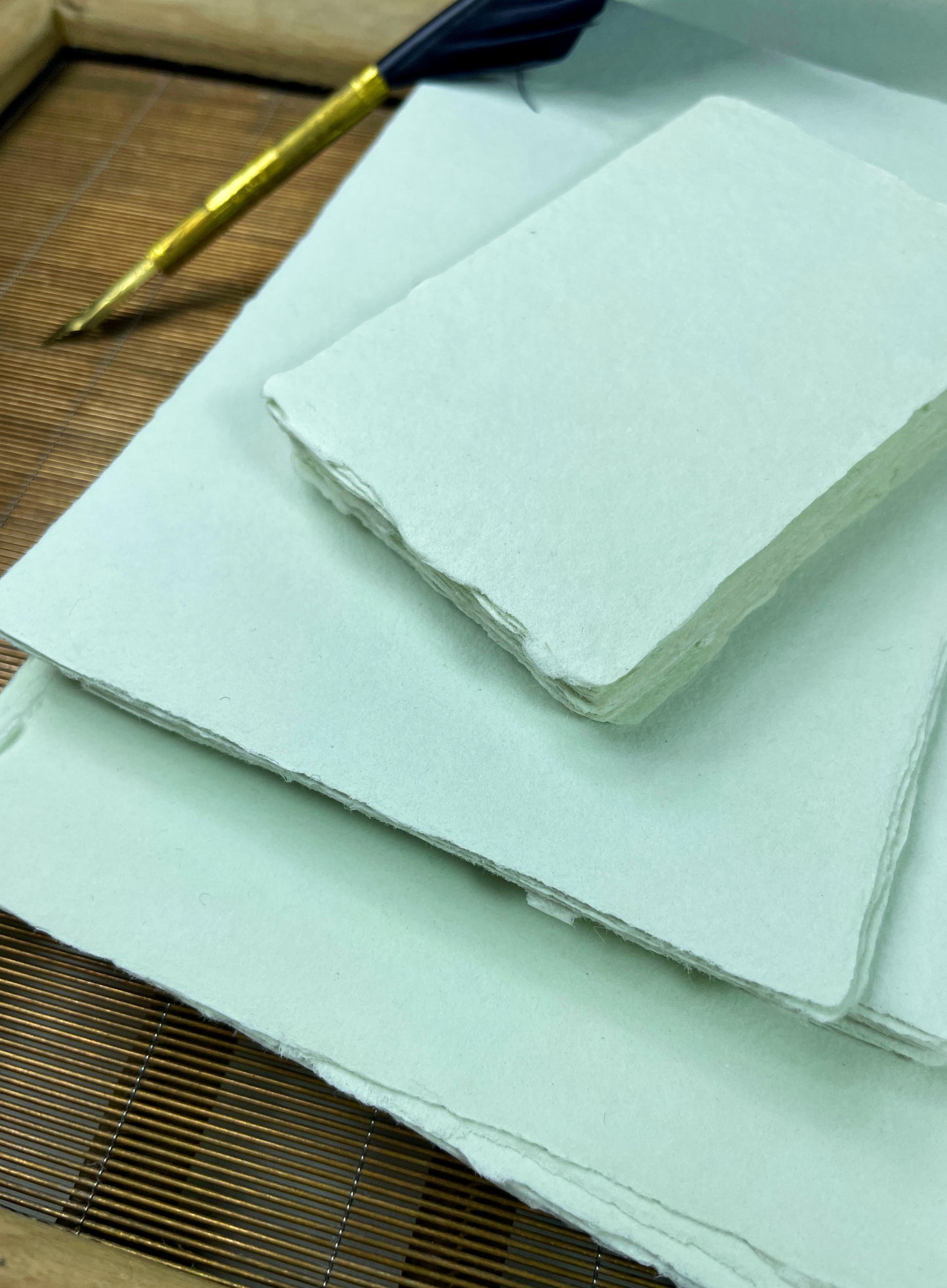 dekoratives Arrangement von mintfarbenem Büttenpapier mit Schreibfeder