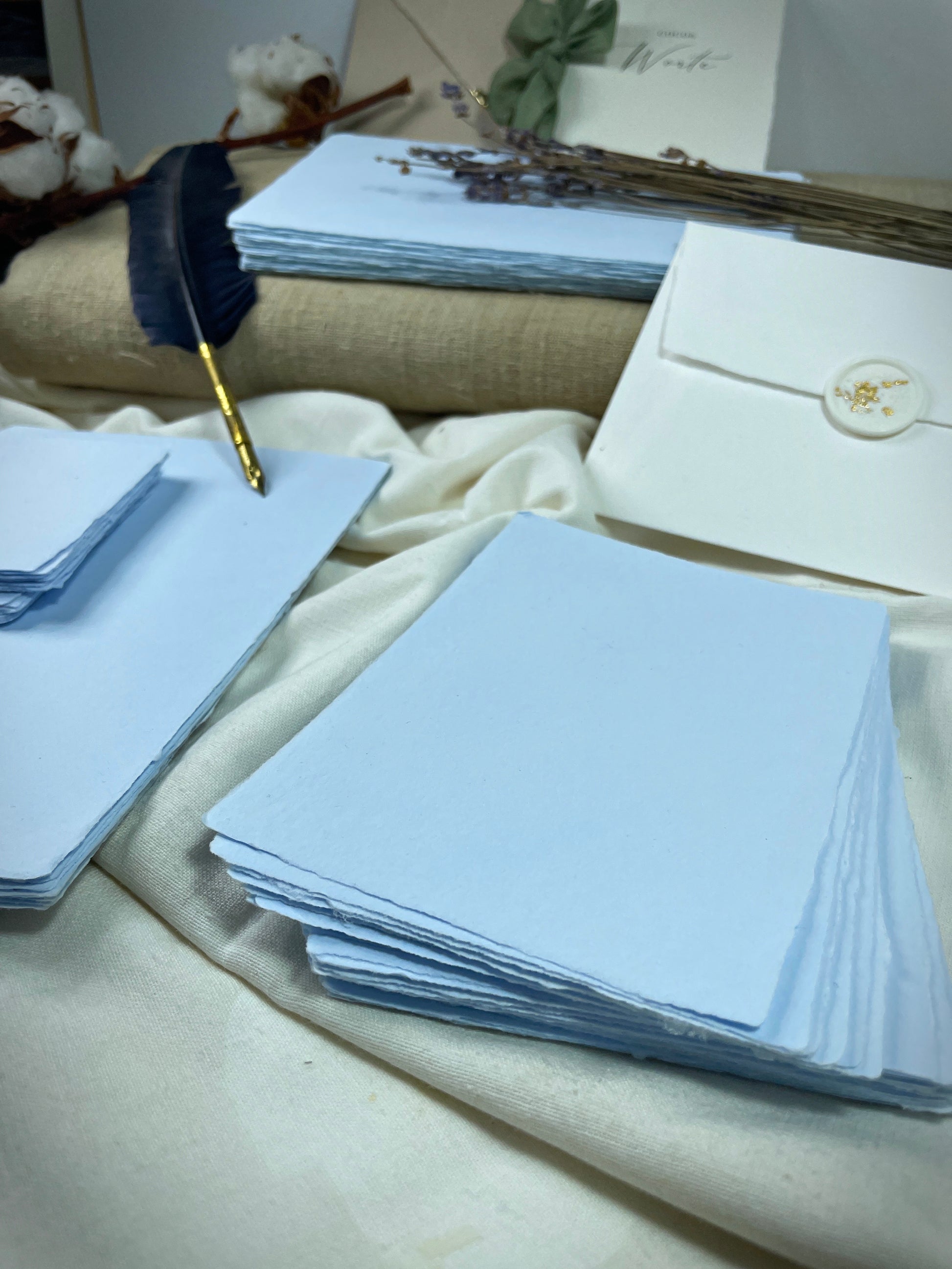 dekoratives Arrangement von blauem, handgeschöpften Büttenpapier mit Schreibfeder