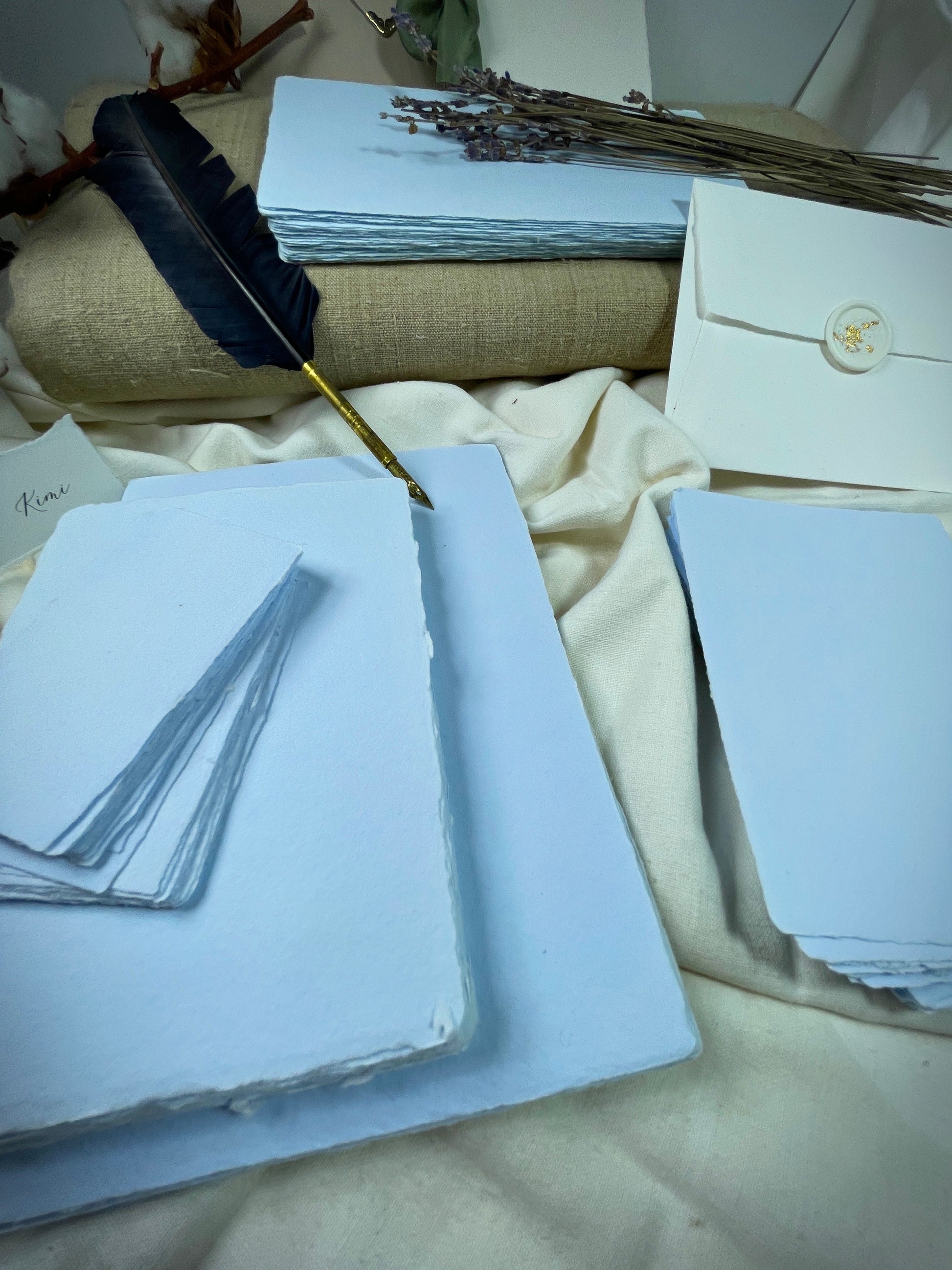 dekoratives Arrangement von blauem, handgeschöpften Büttenpapier mit Schreibfeder