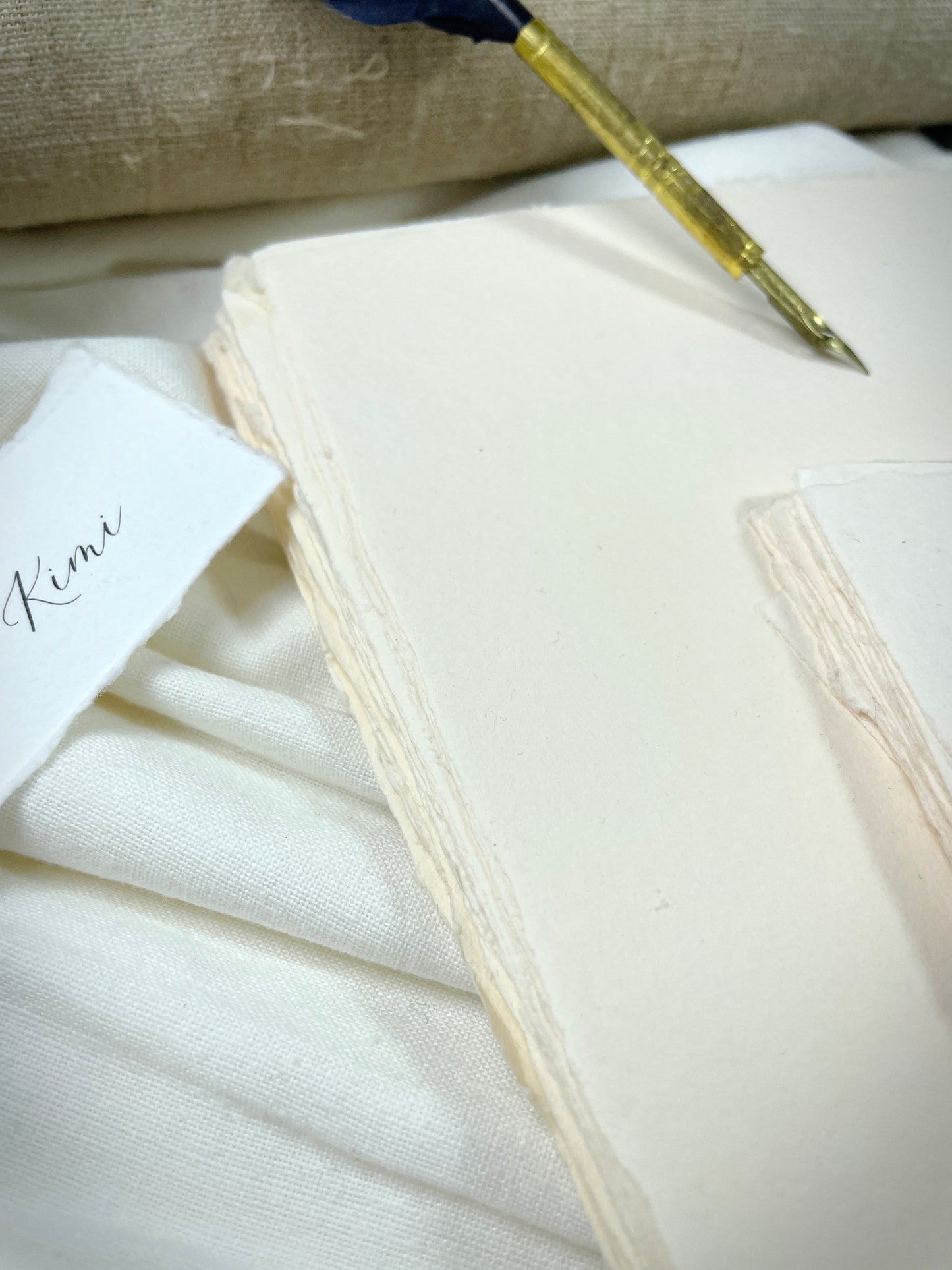 dekoratives Arrangement von cremefarbenem Büttenpapier mit Schreibfeder