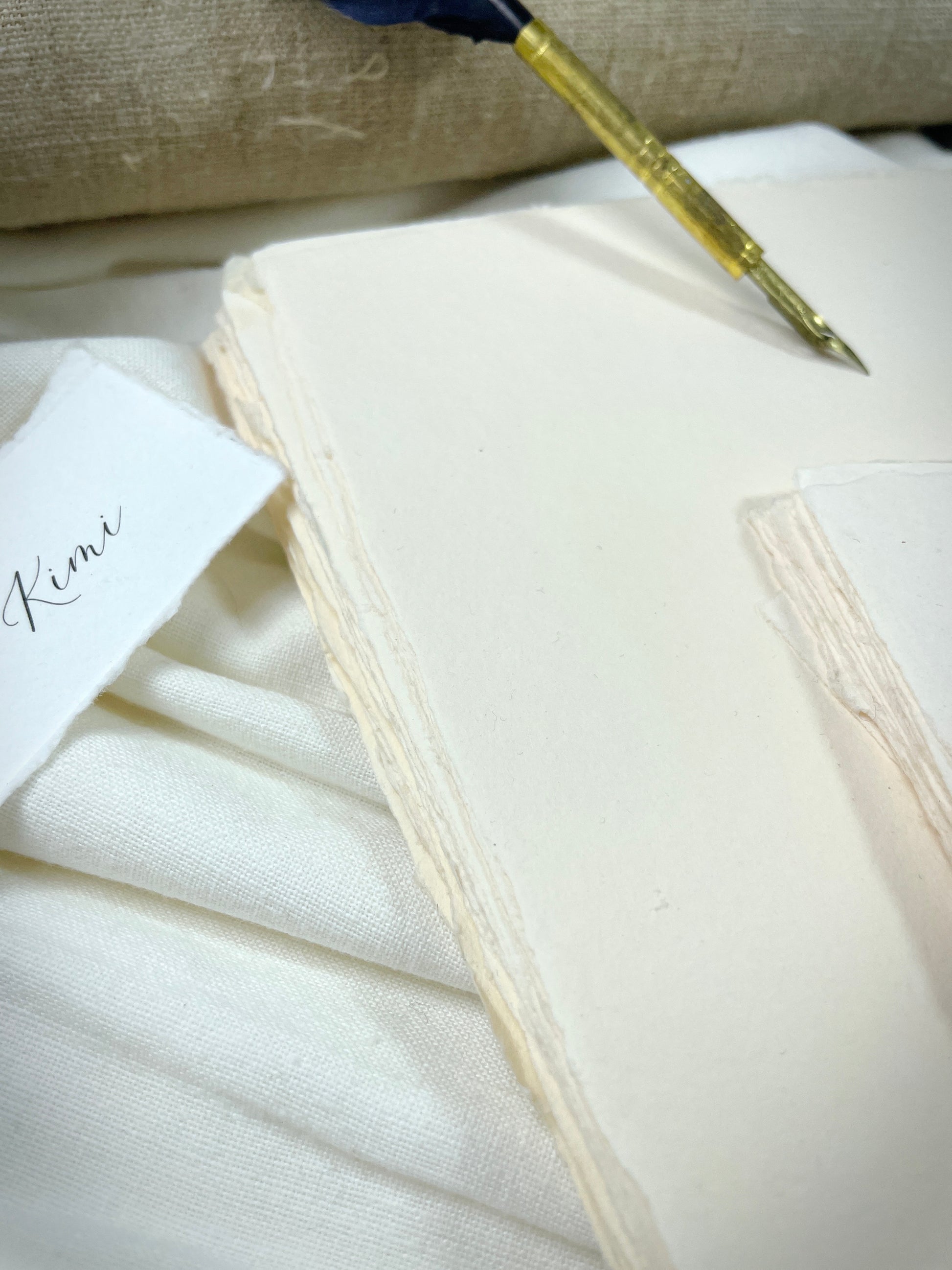 dekoratives Arrangement von cremefarbenem Büttenpapier mit Schreibfeder