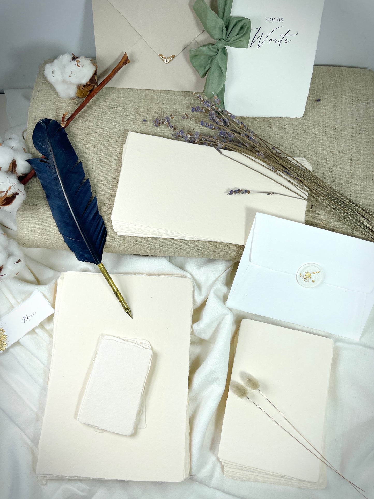 dekoratives Arrangement von cremefarbenem Büttenpapier mit Schreibfeder und Blumen