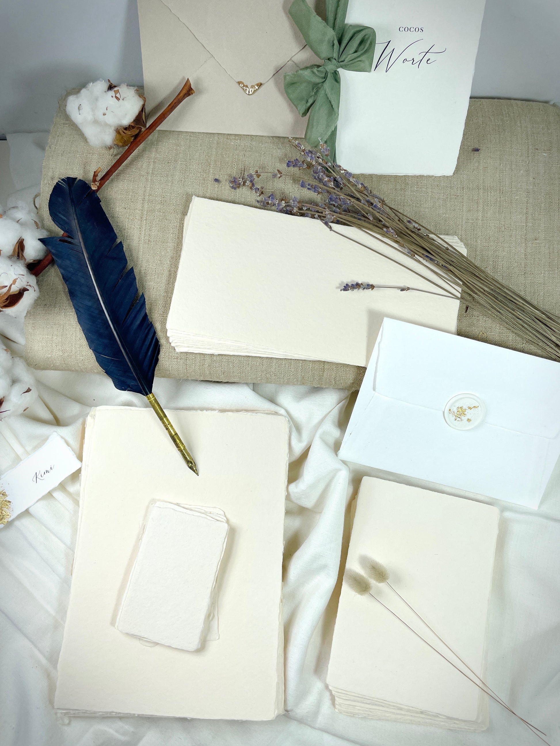dekoratives Arrangement von cremefarbenem Büttenpapier mit Schreibfeder und Blumen
