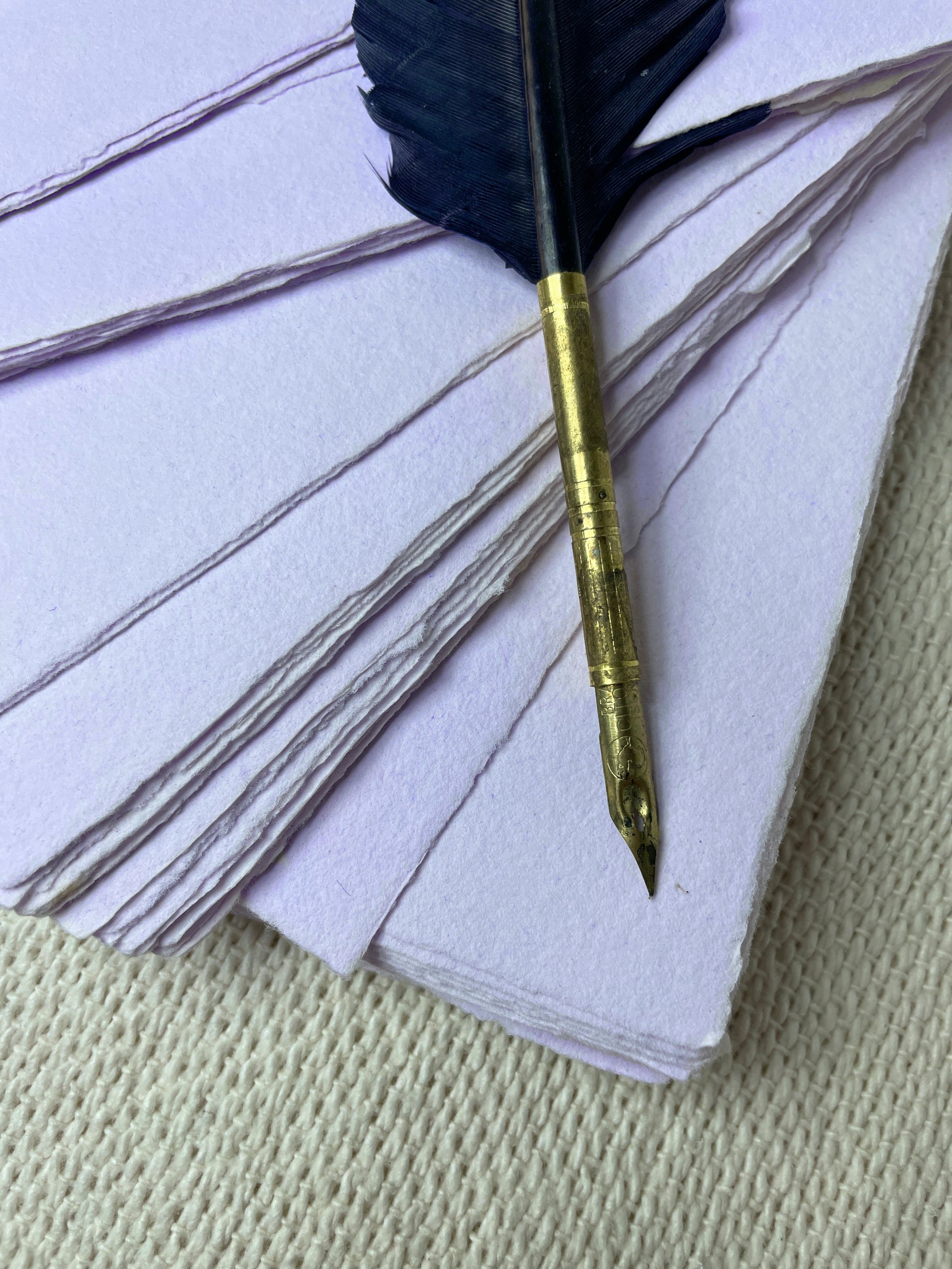 Ein Stapel violettes handgeschöpftes Büttenpapier mit Schreibfeder dekorativ angeordnet