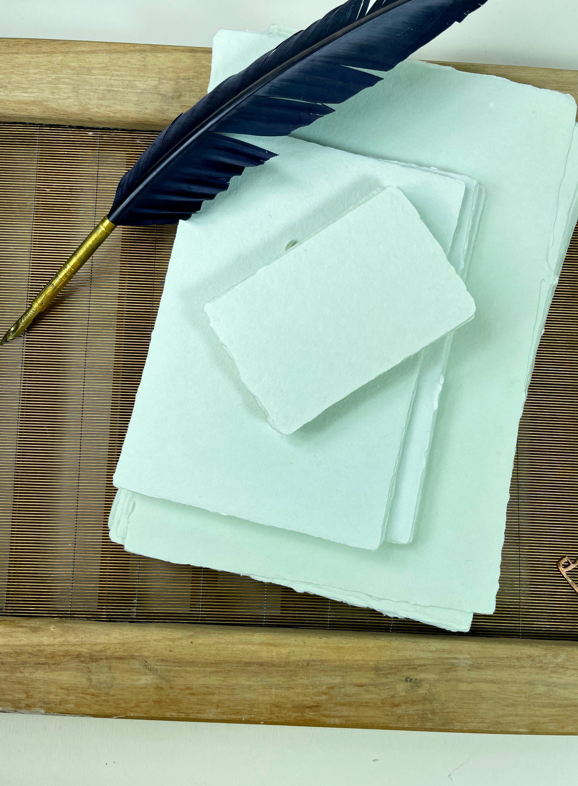 dekoratives Arrangement von mintfarbenem Büttenpapier mit Schreibfeder