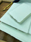 dekoratives Arrangement von mintfarbenem Büttenpapier mit Schreibfeder