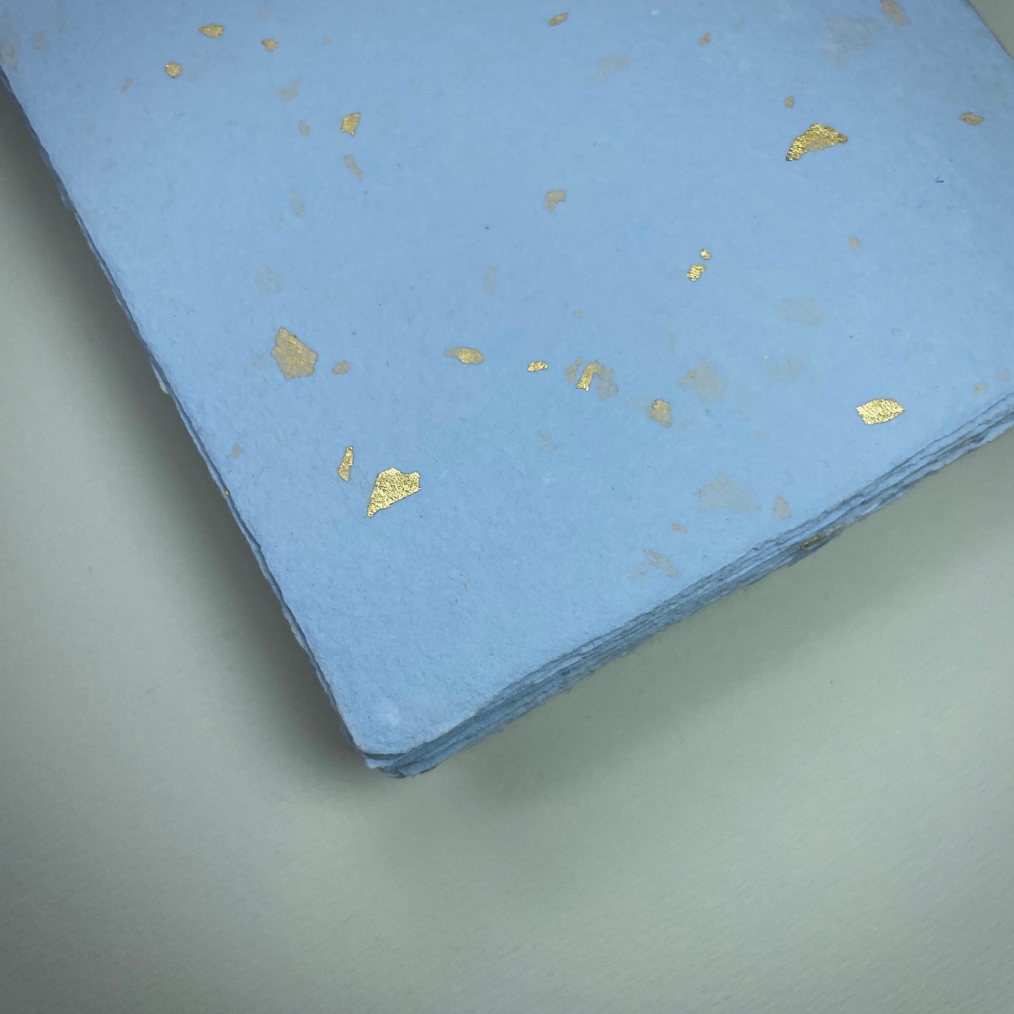Detail eines Büttenpapiers mit eingeschöpften Goldflocken im Farbton babyblau