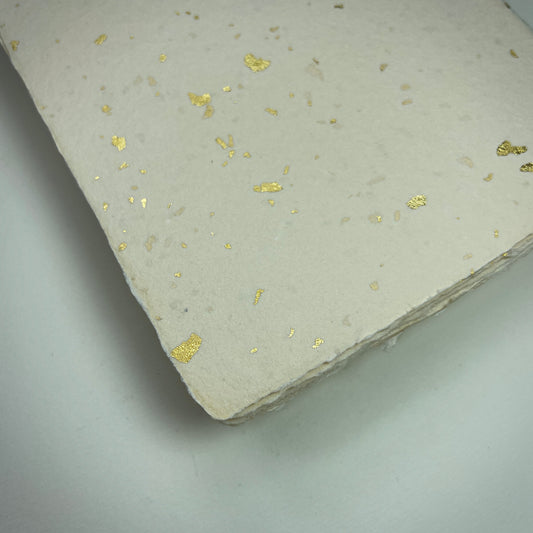 Detail eines Büttenpapiers mit eingeschöpften Goldflocken im Farbton elfenbein