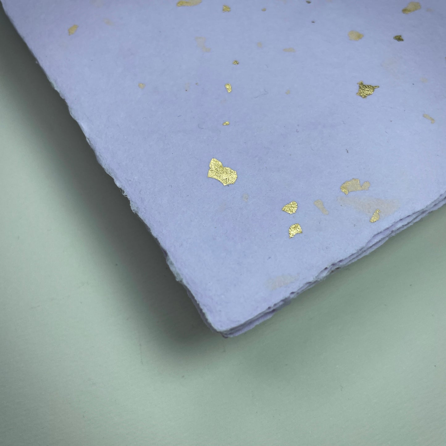 Detail eines Büttenpapiers mit eingeschöpften Goldflocken im Farbton flieder