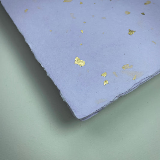 Detail eines Büttenpapiers mit eingeschöpften Goldflocken im Farbton flieder