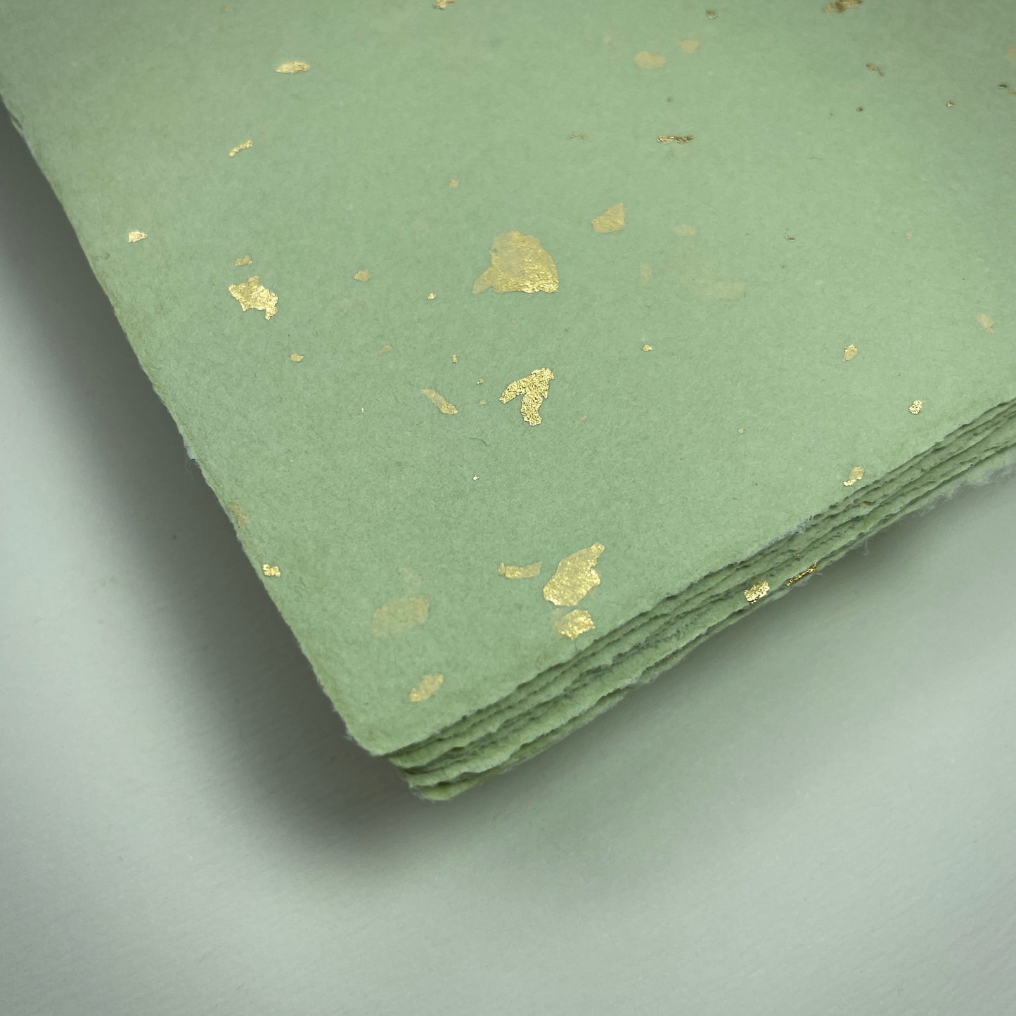 Detail eines Büttenpapiers mit eingeschöpften Goldflocken im Farbton matcha