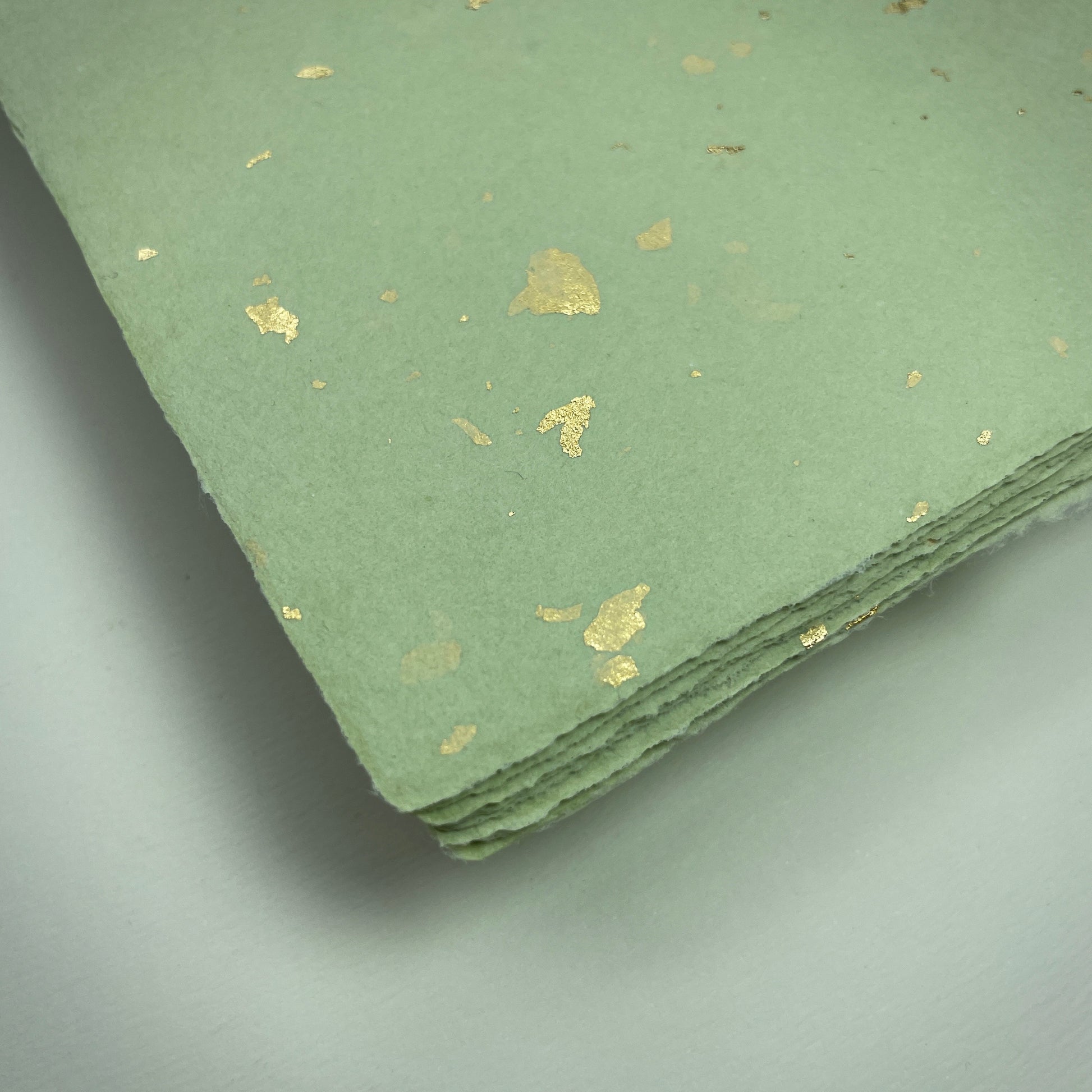 Detail eines Büttenpapiers mit eingeschöpften Goldflocken im Farbton matcha