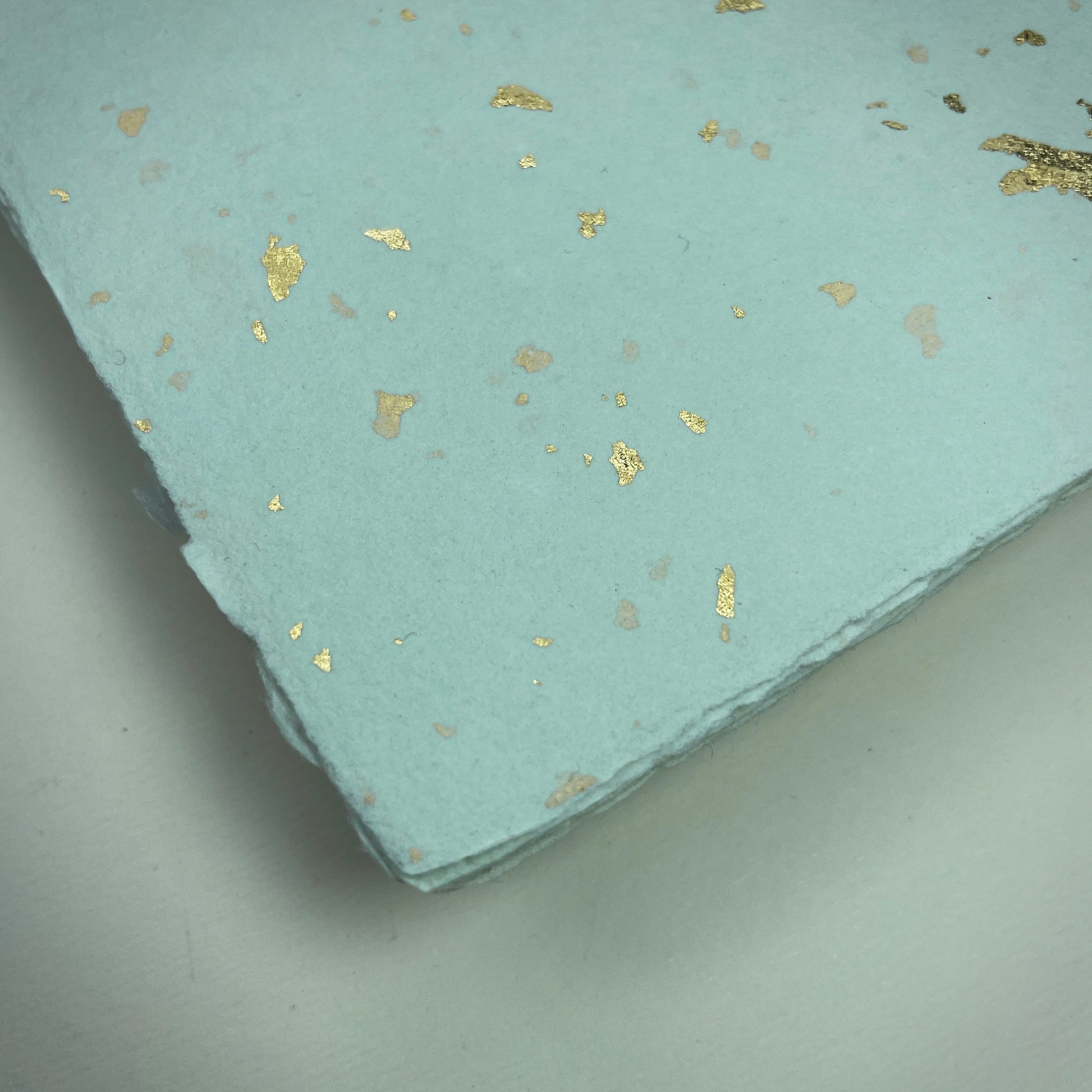 Detail eines Büttenpapiers mit eingeschöpften Goldflocken im Farbton mint