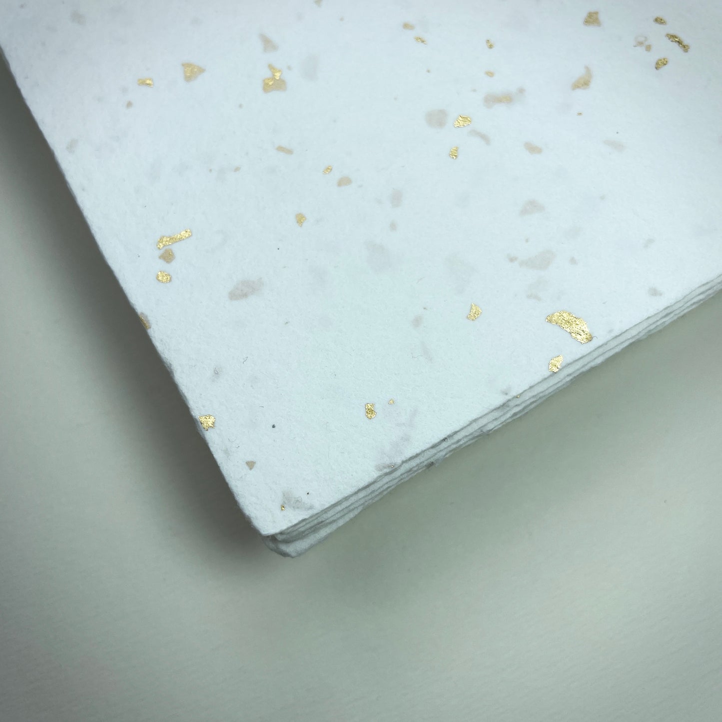 Detail eines Büttenpapiers mit eingeschöpften Goldflocken im Farbton naturweiß