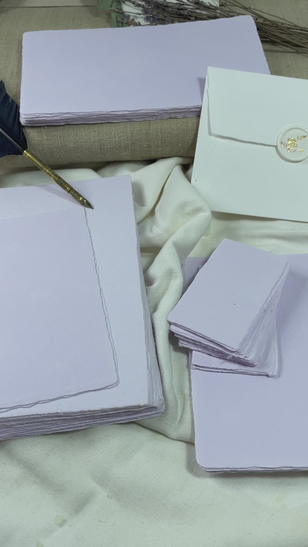 dekoratives Arrangement von violettem Büttenpapier mit Schreibfeder und Blumen