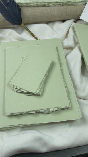 dekoratives Arrangement von grünem Büttenpapier mit Schreibfeder und Blumen
