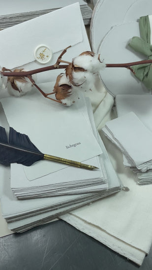 dekoratives Arrangement von grauem Büttenpapier mit Schreibfeder und Blumen