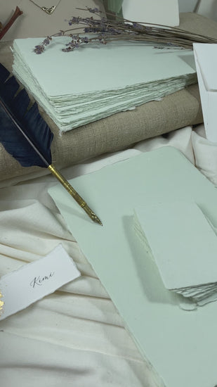 dekoratives Arrangement von mintfarbenem Büttenpapier mit Schreibfeder und Blumen