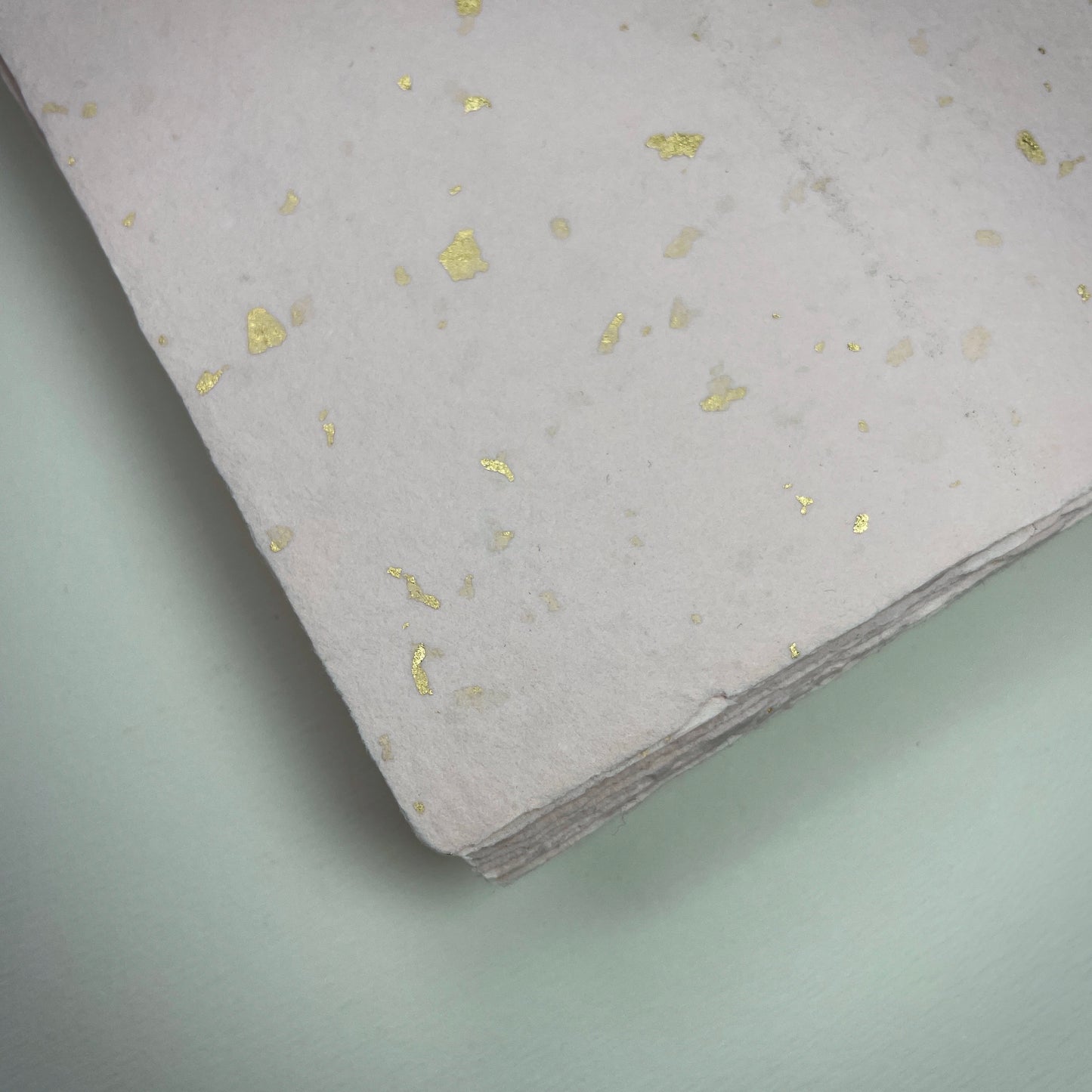 Detail eines Büttenpapiers mit eingeschöpften Goldflocken im Farbton rosé