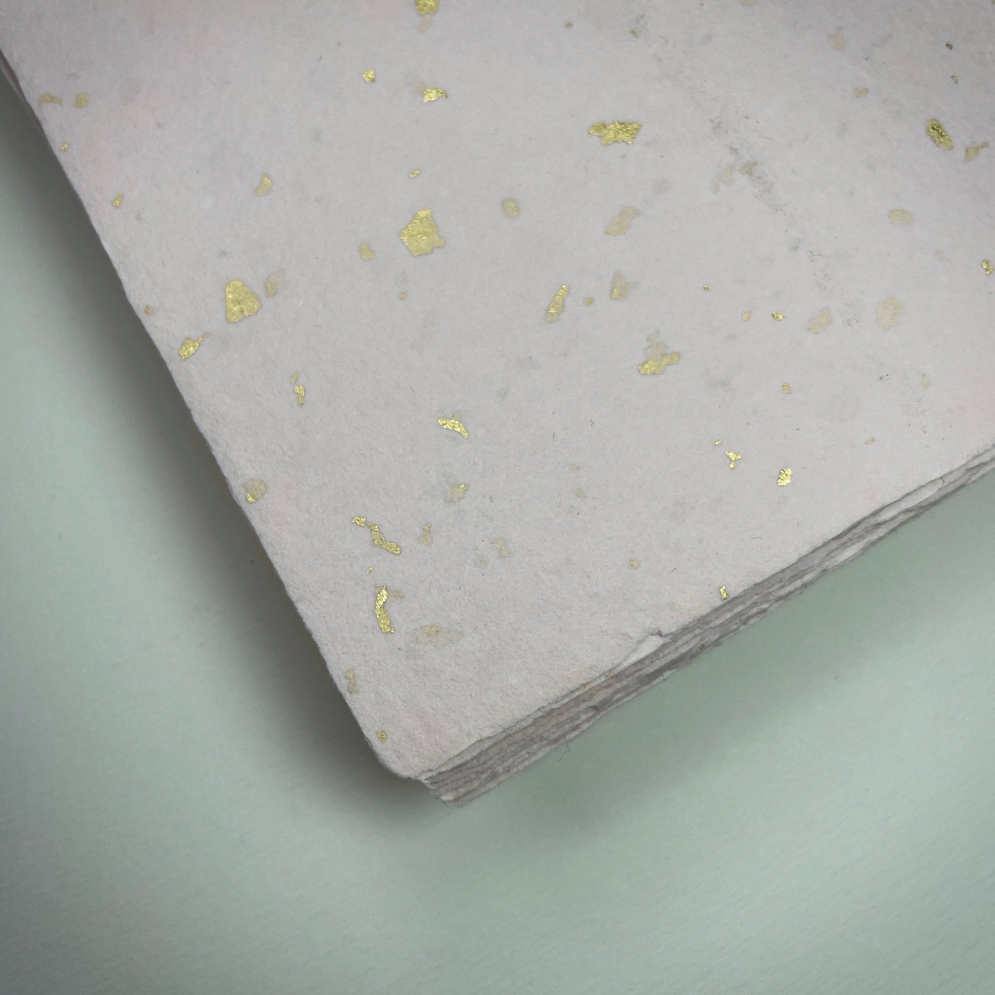 Detail eines Büttenpapiers mit eingeschöpften Goldflocken im Farbton rosé