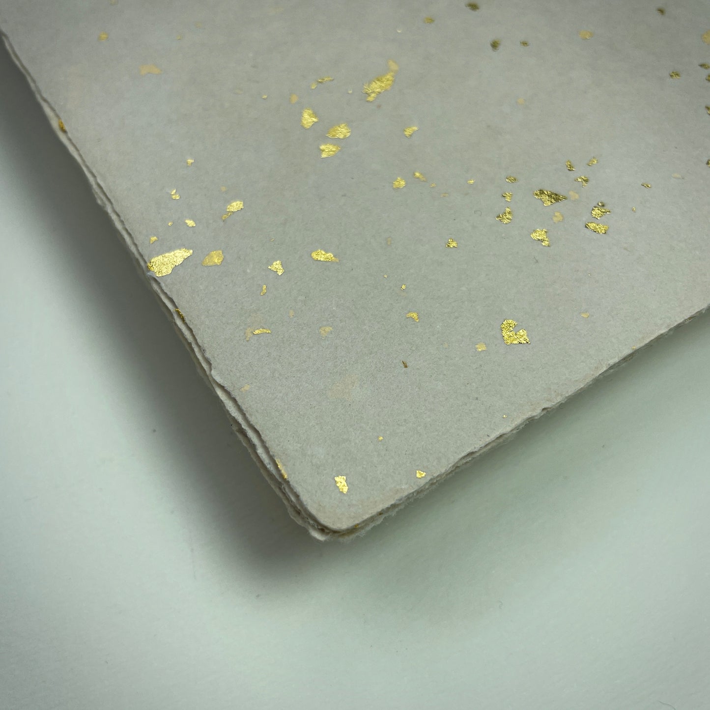 Detail eines Büttenpapiers mit eingeschöpften Goldflocken im Farbton sand