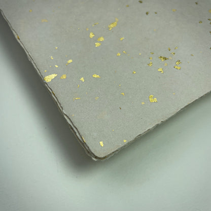 Detail eines Büttenpapiers mit eingeschöpften Goldflocken im Farbton sand