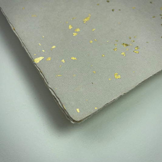 Detail eines Büttenpapiers mit eingeschöpften Goldflocken im Farbton sand